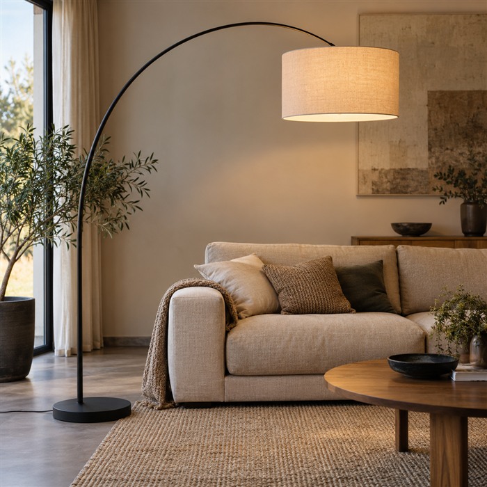 Grote zwarte booglamp met een linnen kap die boven een beige bank hangt.