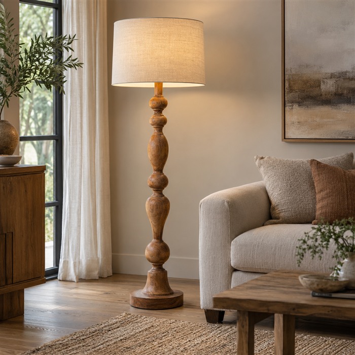 Houten vloerlamp met een gedraaide staander en een lichte stoffen kap naast een bank.