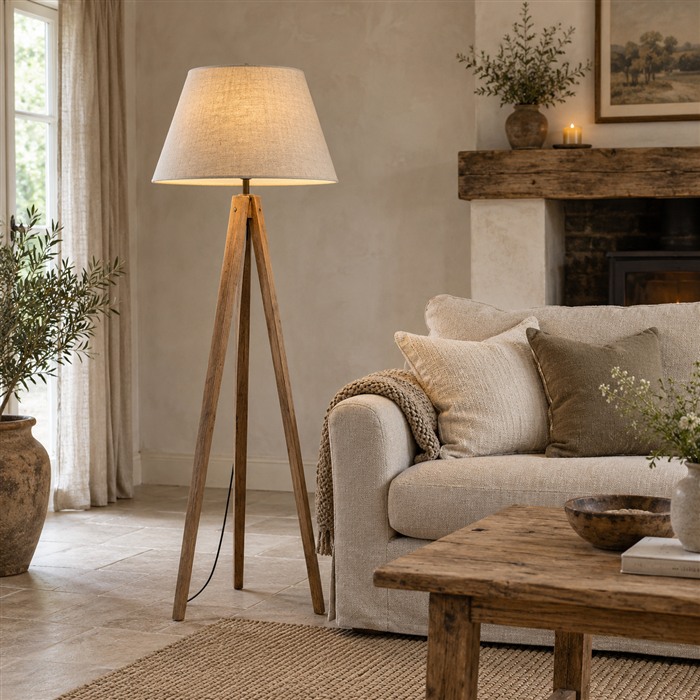 Houten driepoot vloerlamp met een beige linnen kegelkap in een landelijke zithoek.