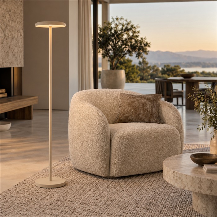 Beige vloerlamp met een schijfvormige kap naast een vrijstaande fauteuil zonder zichtbaar snoer.