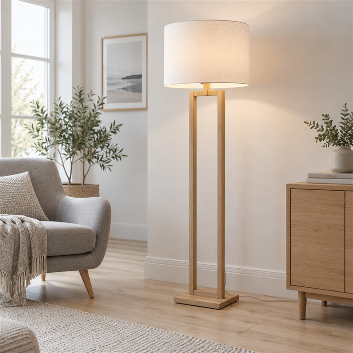 Houten vloerlamp met een witte stoffen kap naast een fauteuil in een lichte Scandinavische woonkamer.