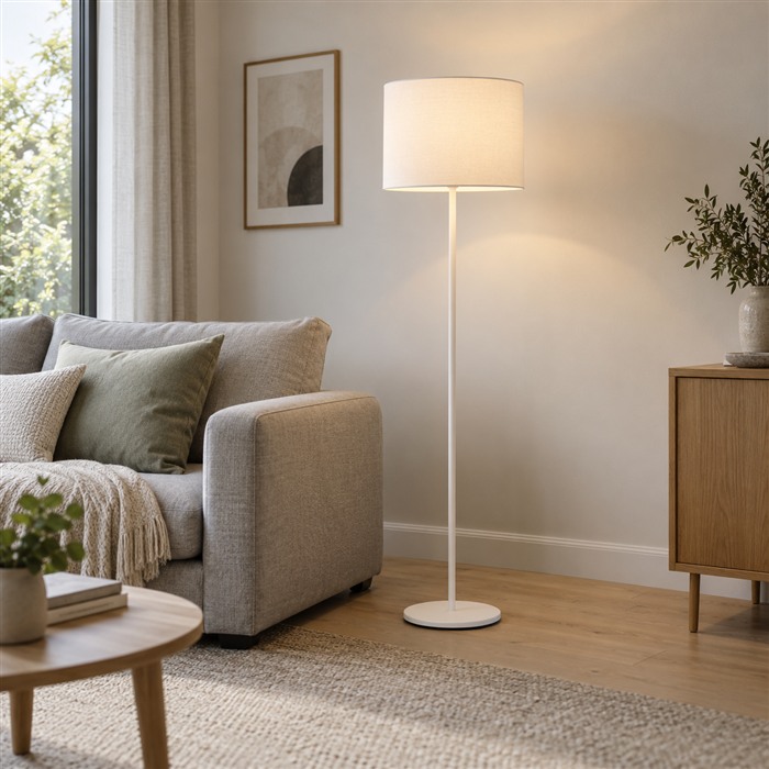Witte vloerlamp met een brede stoffen kap naast een lichtgrijze bank.