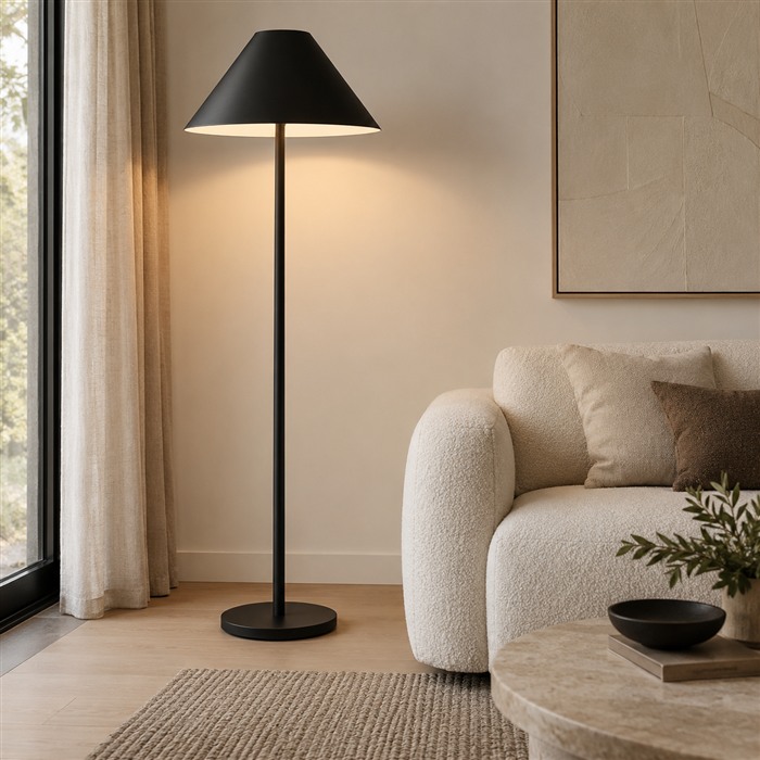 Matte zwarte vloerlamp met een brede kegelkap naast een lichte bank.